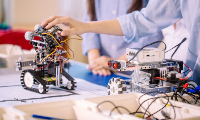 Two robots and two persons, one of which has a hand placed on one of the robots